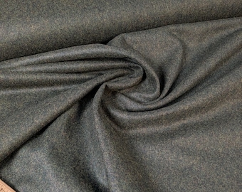 May include: Close-up of a roll of olive green fabric with a textured surface. The fabric is draped and folded, showing the depth and texture of the material. A wooden ruler with the text "Stitch and Stitch" is in the foreground.