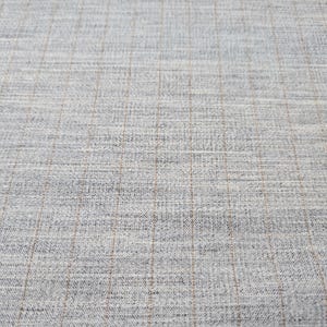 May include: A close-up of a light gray fabric with a subtle brown grid pattern. The fabric has a textured, woven appearance.