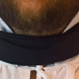 May include: A black neck scarf worn over a white shirt with a white collar.