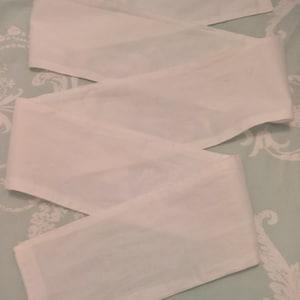 May include: Three white fabric strips, possibly for a headband or hair tie, laid out on a light blue and white floral patterned surface.