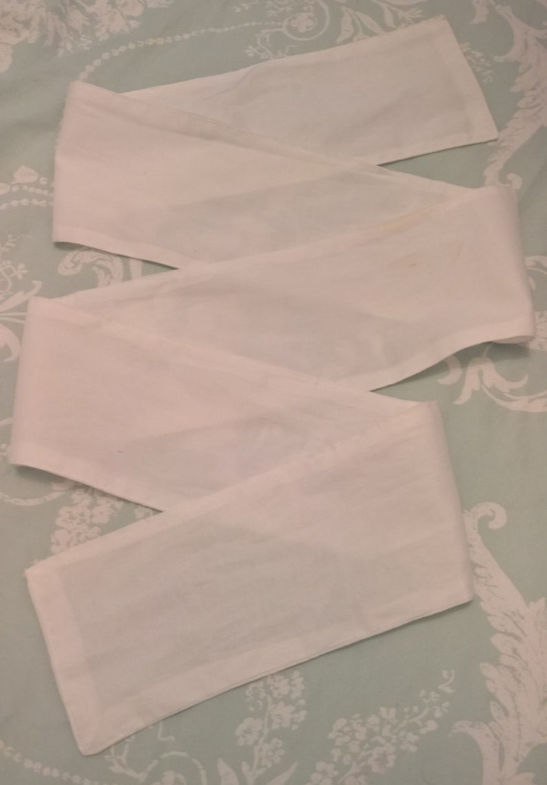 May include: Three white fabric strips, possibly for a headband or hair tie, laid out on a light blue and white floral patterned surface.