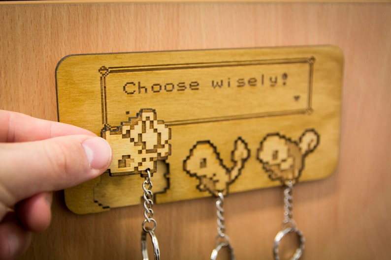 May include: A wooden key holder with a pixelated image of three Pokemon characters. The text "Choose wisely?" is printed on the key holder.