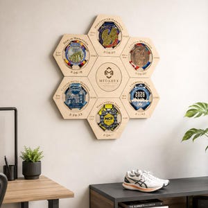 May include: A light-coloured wooden honeycomb-shaped wall display featuring six circular cutouts for medals. Each section is engraved with marathon names, dates, and race times. The centre hexagon displays the Medahex logo and brand text.