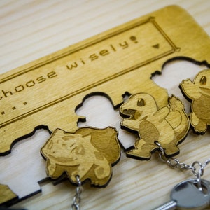 May include: A wooden key holder with a laser-engraved design featuring three Pokemon characters. The holder has a sign that reads "Choose wisely?" and includes three key rings with keys.