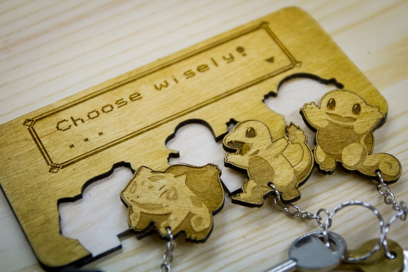 May include: A wooden key holder with a laser-engraved design featuring three Pokemon characters. The holder has a sign that reads "Choose wisely?" and includes three key rings with keys.