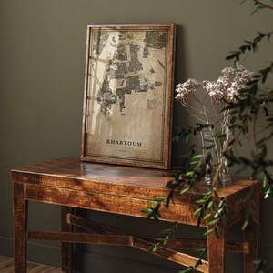 May include: A framed map of Khartoum, Sudan, displayed on a wooden table. The map is in a sepia tone with the city's layout visible. The frame is a dark brown colour. The table is also made of wood and has a rich, warm tone.