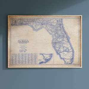 May include: A framed vintage road map of Florida, featuring blue lines on a beige background. The map includes the text "Clason's Road Map of Florida" and a scale in miles. The frame is a light wood color.