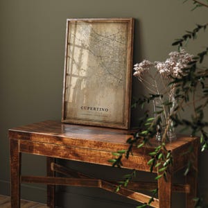 May include: A framed map print of Cupertino, California, in a vintage style. The map is in shades of brown and beige, with the city name and location details at the bottom. The frame is a dark wood color.