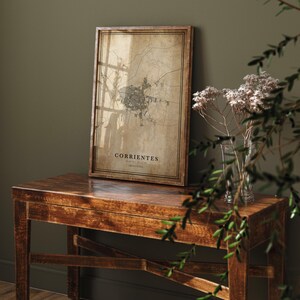 May include: A framed map print of Corrientes, Argentina, displayed on a wooden table. The map has a vintage aesthetic with a sepia tone and detailed city layout. The frame is a dark brown color, and the table has a rich, warm wood finish.