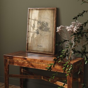 May include: A framed map print of Nadi, Fiji, displayed on a wooden table. The map has a vintage aesthetic with a sepia tone and detailed city outlines. The frame is a dark brown color. The table is also made of wood and has a dark brown finish.