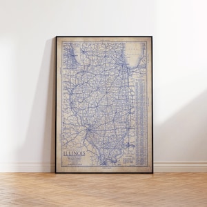 May include: A framed vintage map of Illinois, featuring a detailed blue road network against a beige background. The map includes the state's name and other text at the bottom. The frame is black, and the map is displayed on a wooden floor.