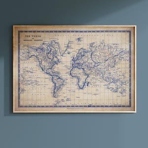May include: A framed vintage world map in blue ink on a tan background. The map is labelled "THE WORLD" and "MERCATOR'S PROJECTION". The map is enclosed in a light brown wooden frame. The map shows continents, countries, and oceans.