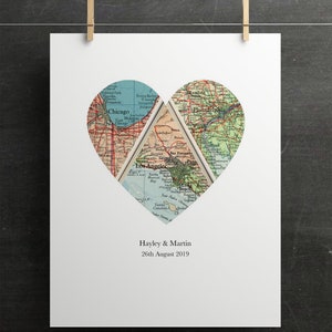 May include: A white print featuring a heart-shaped design composed of vintage map segments. The maps highlight Chicago, Los Angeles, and Philadelphia. The names "Hayley & Martin" and the date "26th August 2019" are printed below the heart. The print is held by two gold-colored clips.