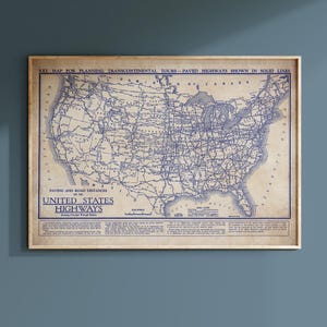 Op de afbeelding: Een ingelijste vintage kaart van de Verenigde Staten, met snelwegen in blauw tegen een bruine achtergrond. De kaart bevat tekst die aangeeft dat deze bedoeld is voor het plannen van transcontinentale tours. De lijst is lichtbruin.