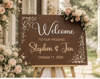 May include: A rectangular dark brown wooden wedding sign on a light wooden easel. The sign features laser-cut floral corners and white and gold lettering that reads: Welcome TO OUR WEDDING Stephen & Jen October 11, 2025. The sign is decorated with pink and white roses.