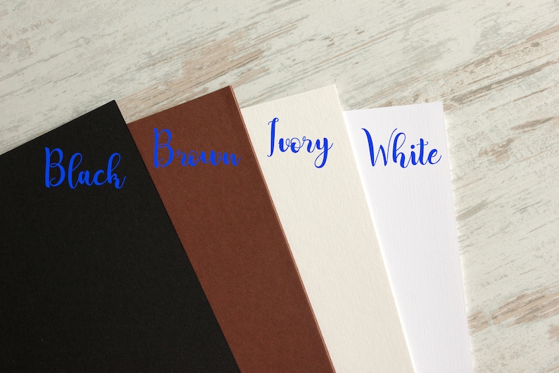 May include: Four samples of cardstock in different colors: black, brown, ivory, and white. The colors are labeled in blue cursive writing.
