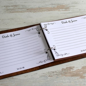 May include: A brown wooden recipe book with a white paper insert. The book is open to show the lined pages. The book has a decorative border with the text "Dutch & Jeanne" and the date "11-11-18".
