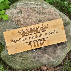 Könnte beinhalten: Ein Schneidebrett aus Holz mit einem lasergravierten Design von Küchenutensilien und dem Text "Meilleur papa du monde".