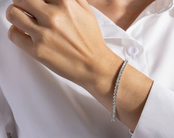 May include: A silver tennis bracelet with small, clear stones.