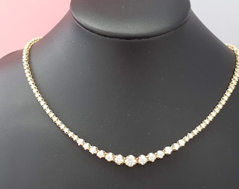 May include: A gold necklace with a row of round diamonds. The necklace is on a black display stand.