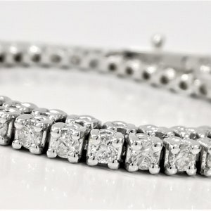 May include: A silver tennis bracelet with a row of small, clear, square-shaped diamonds.