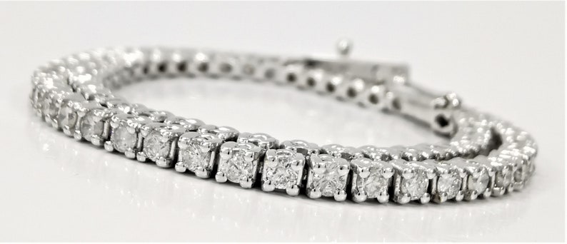 May include: A silver tennis bracelet with a row of small, clear, square-shaped diamonds.