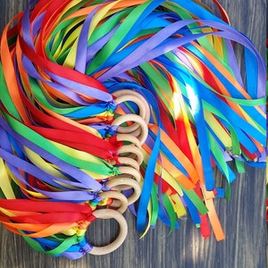 Può includere: Bacchette di nastro arcobaleno con anelli di legno. I nastri sono di colore rosso, arancione, giallo, verde, blu, indaco e viola. Gli anelli di legno sono attaccati ai nastri e vengono utilizzati per tenere le bacchette.