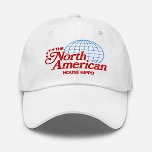 Pode incluir: Boné de beisebol branco com um logotipo bordado em vermelho e azul que diz "The North American House Hippo" com um gráfico de globo.