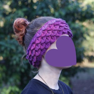 May include: Purple crocheted headband with a scale pattern. The headband is worn by a person with brown hair.