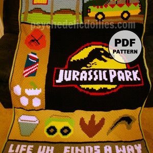 Puede incluir: Una manta de crochet con temática de Jurassic Park. La manta es negra con un logotipo de Jurassic Park amarillo, rojo y blanco. La manta también presenta un jeep verde, una huella de dinosaurio y el texto "Life uh... finds a way".