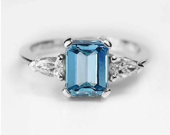 May include: A silver ring with a large, rectangular, blue gemstone surrounded by two smaller, pear-shaped, clear gemstones.