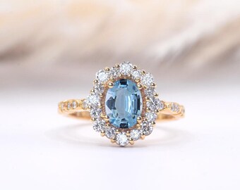 May include: A gold ring with a large oval aquamarine gemstone surrounded by a halo of smaller diamonds. The ring has a delicate band with additional diamonds.