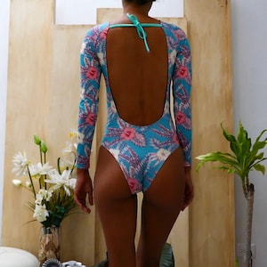 May include: A blue and pink floral print swimsuit with long sleeves and a low back. The swimsuit has a turquoise string tie at the back.