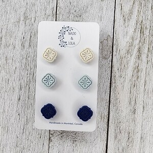 May include: A card of six stud earrings in cream, light blue, and navy blue. Each earring has a floral pattern. The card has the text "Nado & Lola" and "Handmade in Montréal, Canada". The earrings are suitable for everyday wear.