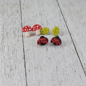 May include: A set of six small, colourful earrings featuring red and white mushrooms, red and black ladybirds, and green leaves. The earrings are made of polymer clay and are perfect for adding a touch of whimsy to any outfit.