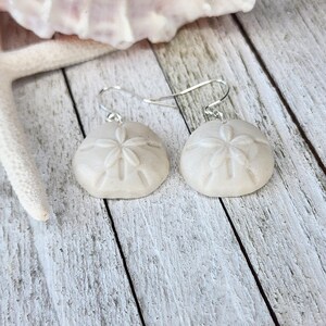 Peut inclure: Une paire de boucles d'oreilles en argent avec des breloques en forme de dollar des sables blancs. Les dollars des sables ont un design en relief détaillé.