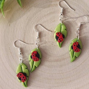 May include: A pair of silver earrings with green leaf charms and red and black ladybug accents.