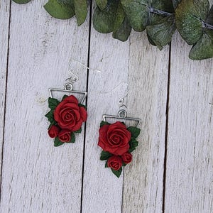 Könnte beinhalten: Ein Paar silberne Ohrhänger mit roten Rosenakzenten. Die Rosen sind aus Polymer Clay gefertigt und in einer dreieckigen Form angeordnet.