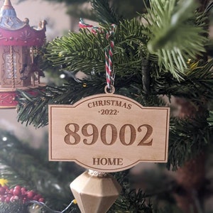 May include: A wooden Christmas ornament with the text "Christmas 2022" and the number "89002" on it. The ornament also has the word "Home" on it and is hanging from a Christmas tree.