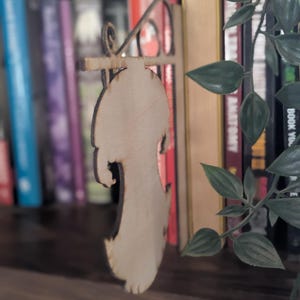 May include: A wooden sign with a blank space for text. The sign is hanging from a metal bracket and is attached to a bookshelf.