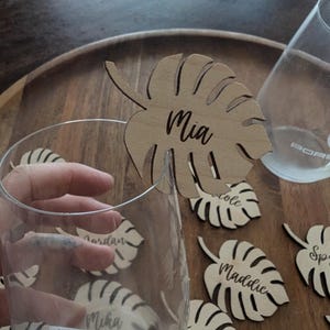 May include: Wooden tropical leaf place cards with names written on them. The names include Mia, Jordan, Mika, Maddie, Cole, and Ailyn.