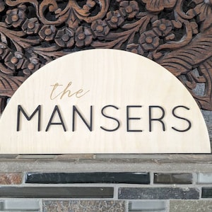 May include: A wooden sign in the shape of a half-circle with the text "the MANSERS" in black lettering and "the" in gold lettering.