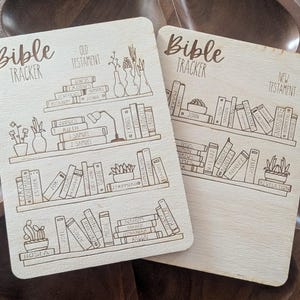 May include: Two wooden Bible tracker boards with a shelf design. The left board is labeled "Bible Tracker" and "Old Testament" and features a list of books from the Old Testament. The right board is labeled "Bible Tracker" and "New Testament" and features a list of books from the New Testament.