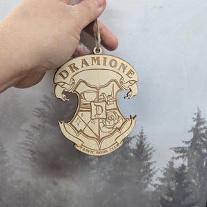 May include: Wooden ornament with a crest featuring a cup, a rose, and the text "Dramione Fanfic Book Club".
