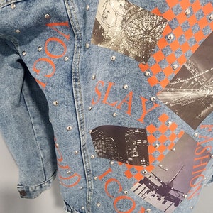 May include: A light blue denim jacket with silver studs and orange printed text that says "VOGUE", "SLAY", "ICON", and "FASHION". The jacket has several patches with images of a chandelier, a city skyline, and an airplane.