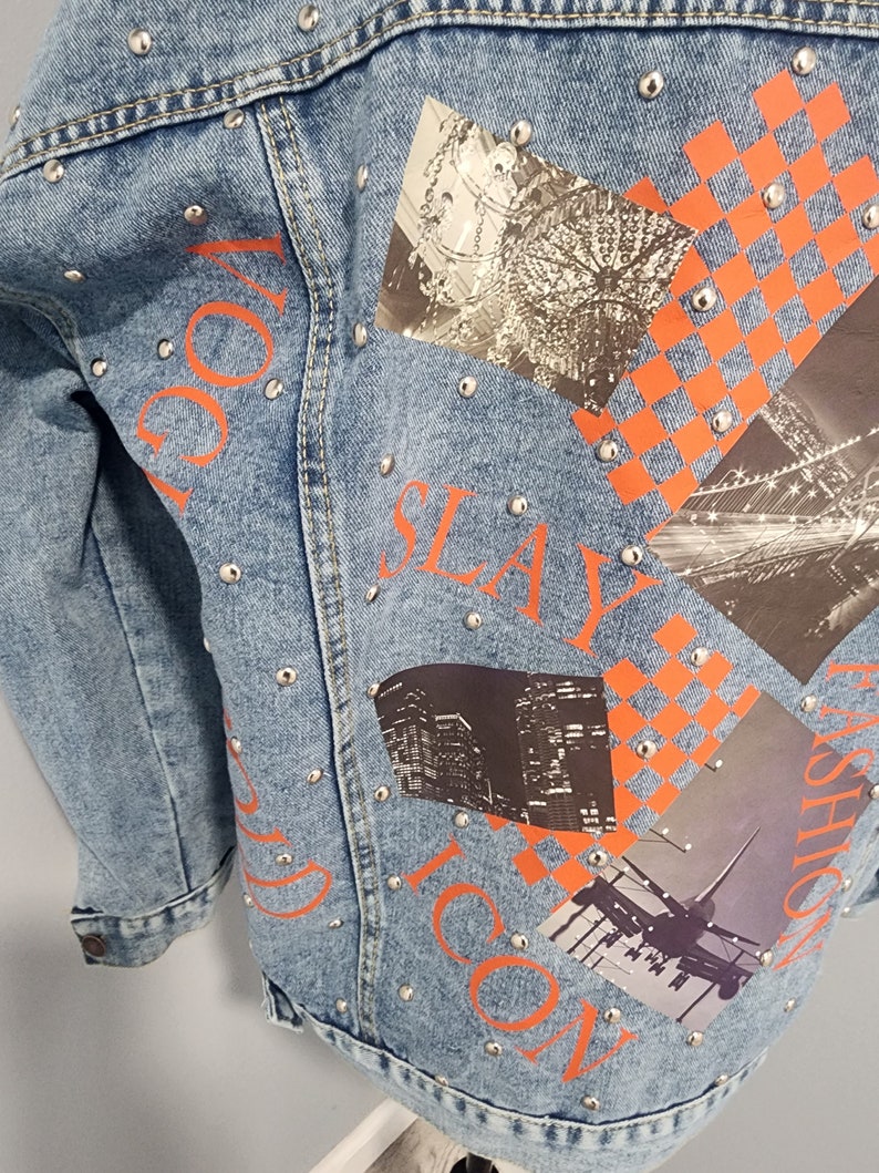 May include: A light blue denim jacket with silver studs and orange printed text that says "VOGUE", "SLAY", "ICON", and "FASHION". The jacket has several patches with images of a chandelier, a city skyline, and an airplane.