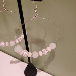 May include: A pair of silver hoop earrings with white and clear beads. The beads are round and have a sparkly finish.