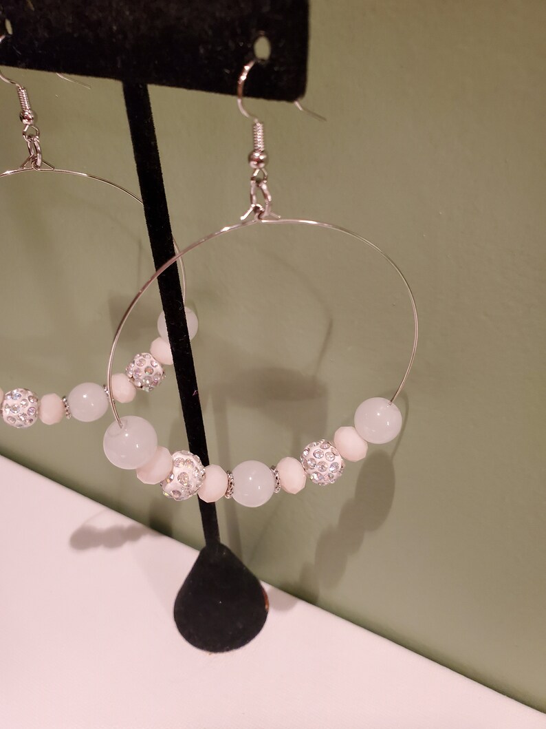 May include: A pair of silver hoop earrings with white and clear beads. The beads are round and have a sparkly finish.