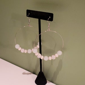 May include: A pair of silver hoop earrings with white and light blue beads. The beads are accented with silver rhinestones.
