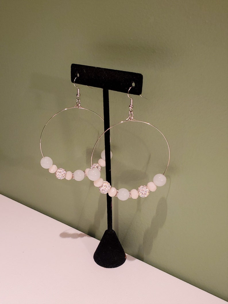 May include: A pair of silver hoop earrings with white and light blue beads. The beads are accented with silver rhinestones.
